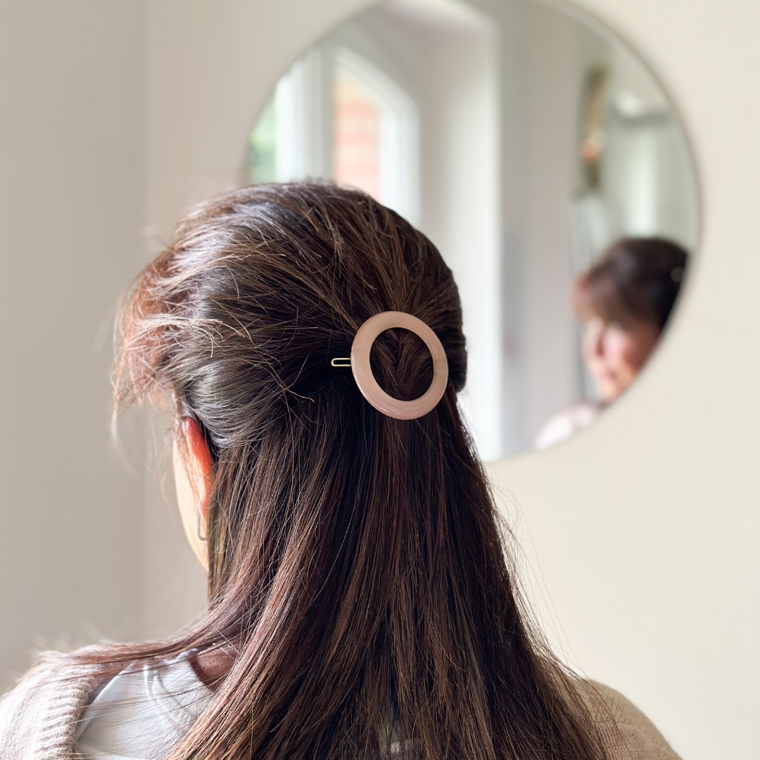 Femme de dos portant dans ses cheveux une barrette à cheveux ronde rose pâle de la marque Bachca.