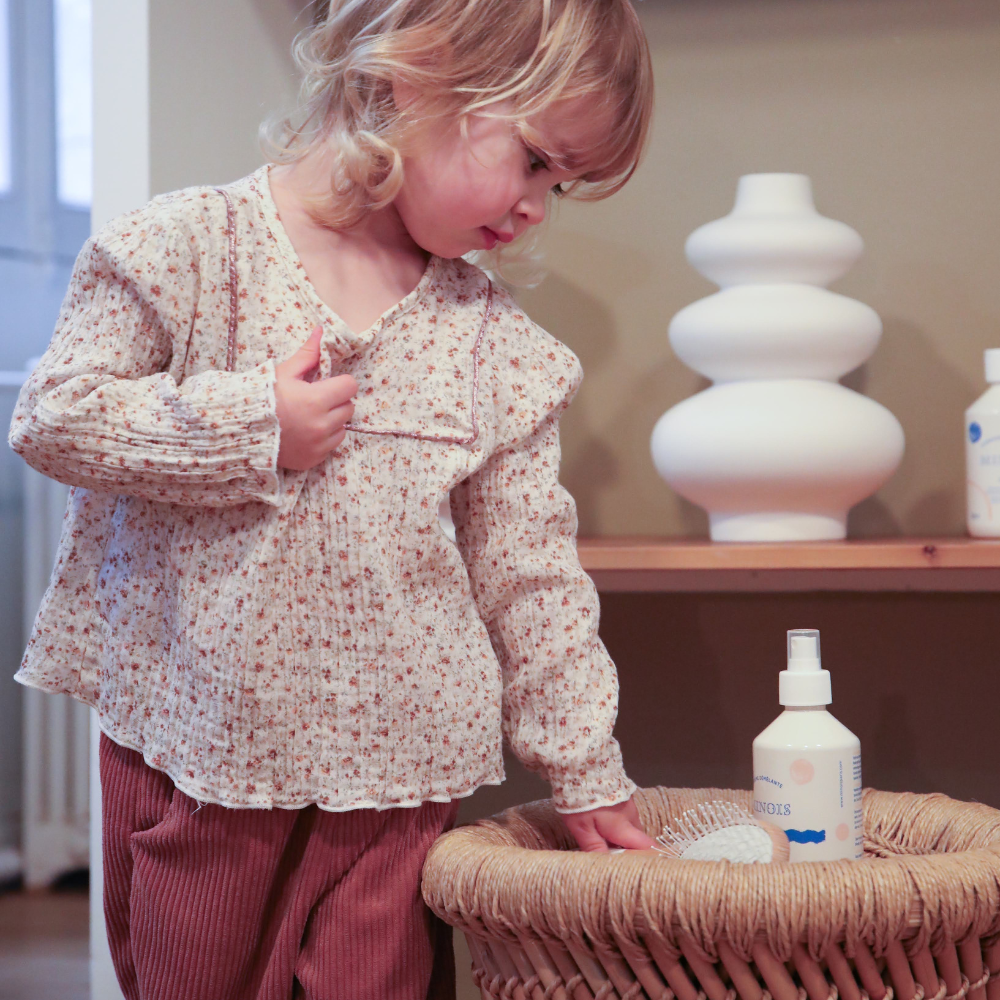 Petite fille qui regarde attentivement une brûme pour les cheveux et tient une brosse à cheveux Bachca dans ses mains.