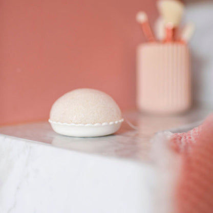 Éponge konjac Bachca posée sur son support blanc en céramique, accessoire beauté naturel pour nettoyer et exfolier le visage en douceur.