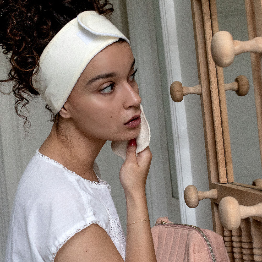 Femme portant le bandeau de démaquillage en coton Bachca, se nettoyant le visage devant un miroir en bois.
